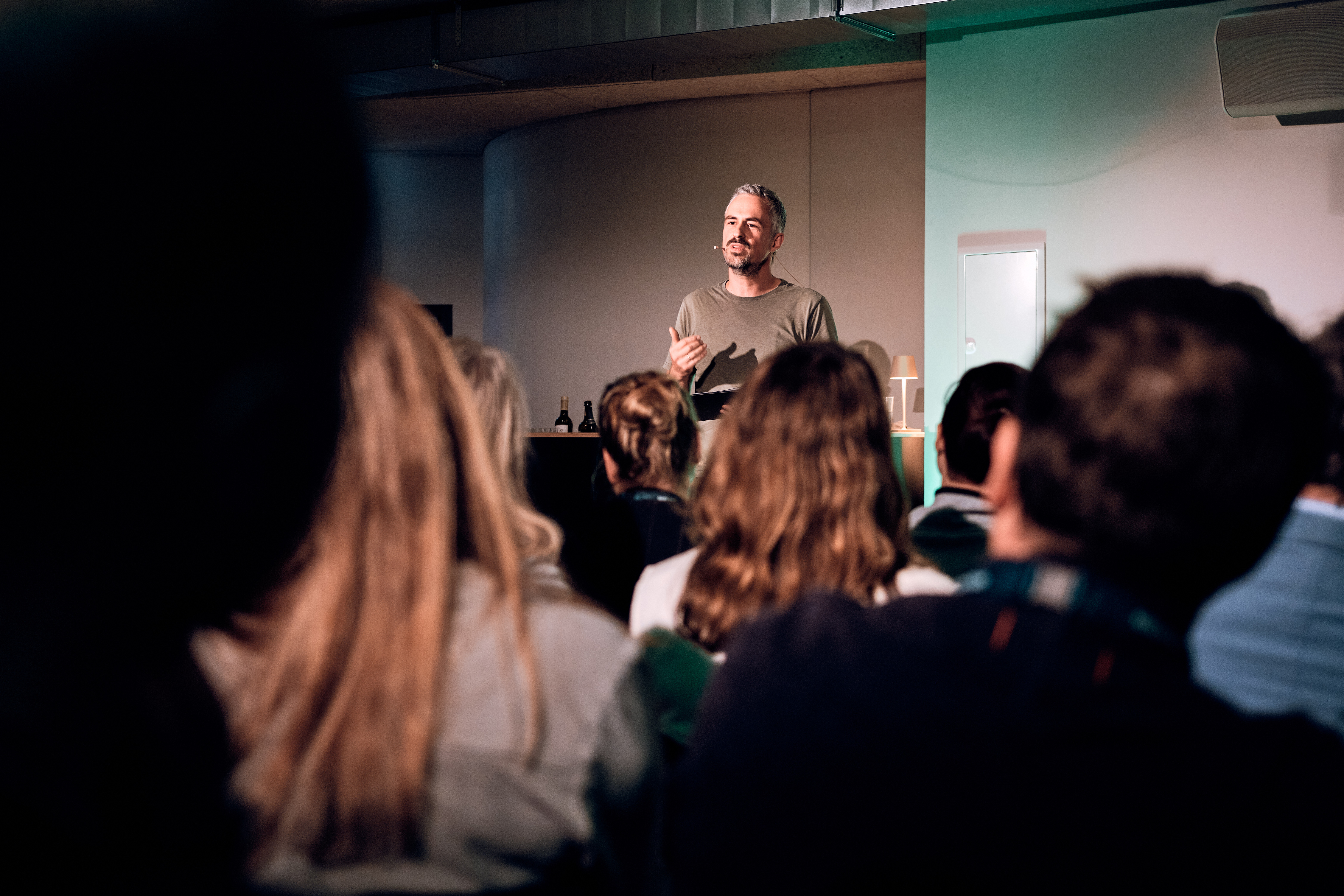 Ein Mann steht und spricht zu einem Publikum, das in einem Raum sitzt, und hält eine Präsentation oder einen Vortrag.